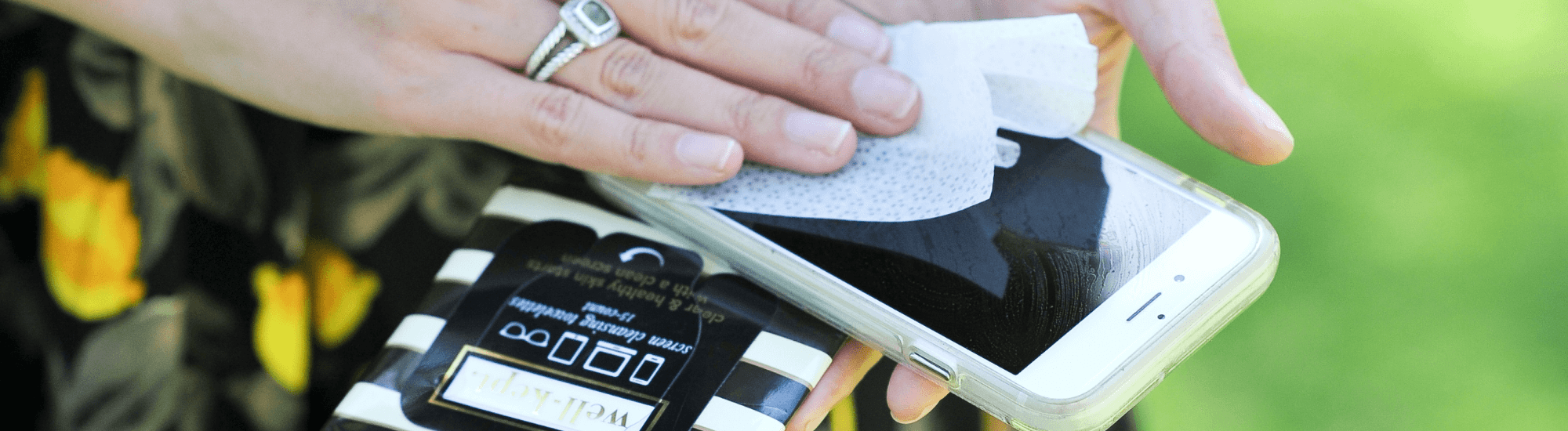 up close image of woman's hand wiping phone with Well-Kept screen wipes.