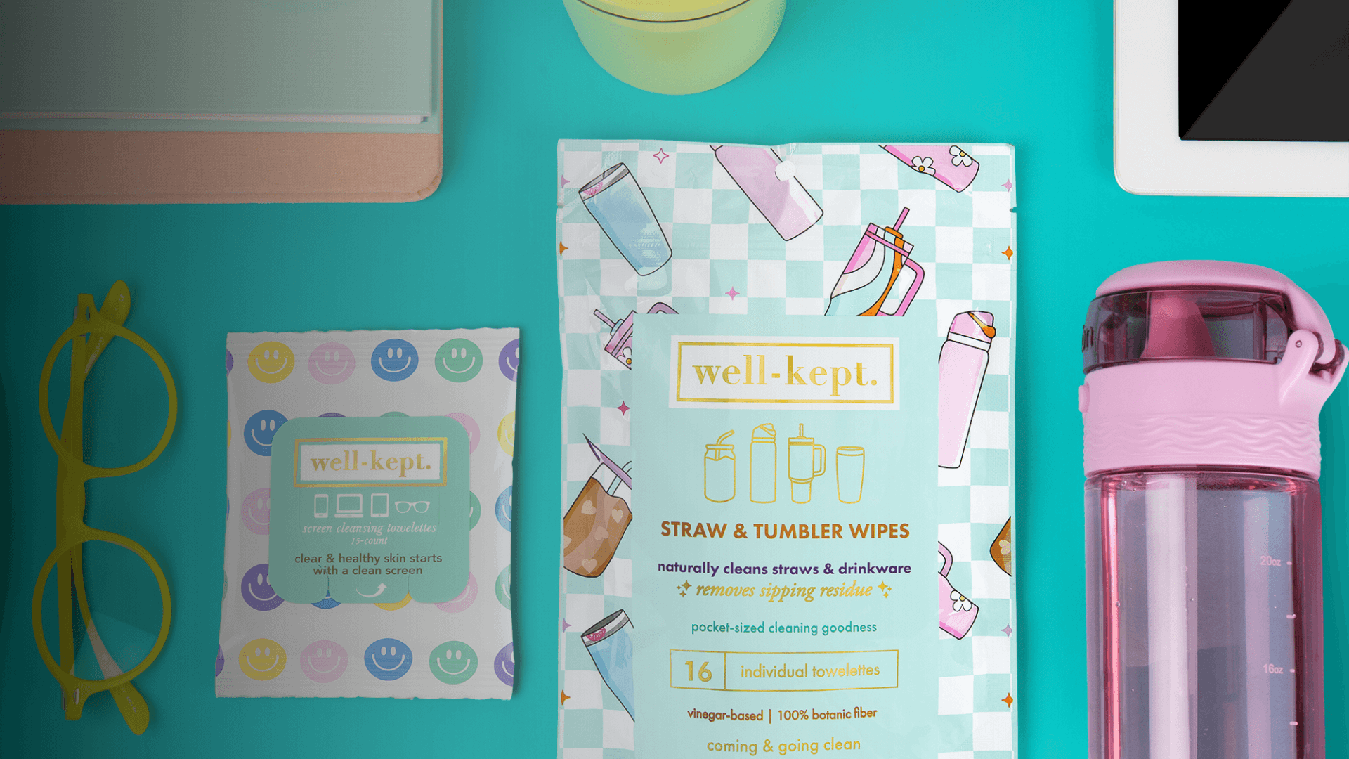 A flat lay of cleaning wipes, a pink tumbler, yellow glasses, and other items on a teal surface.