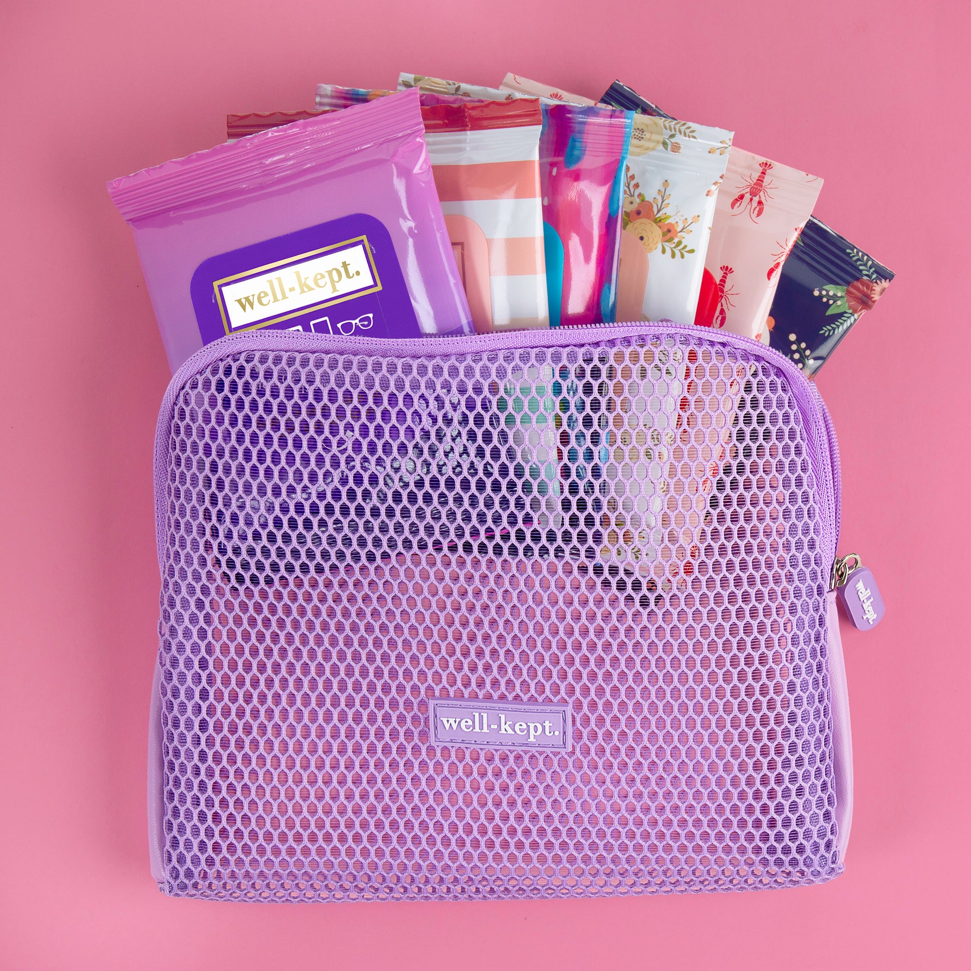 The purple Mesh Tech Pouch, made of lightweight nylon mesh, holds colorful packaged wipes and sits on a pink background—ideal as a travel wipe pouch for carrying on-the-go essentials.