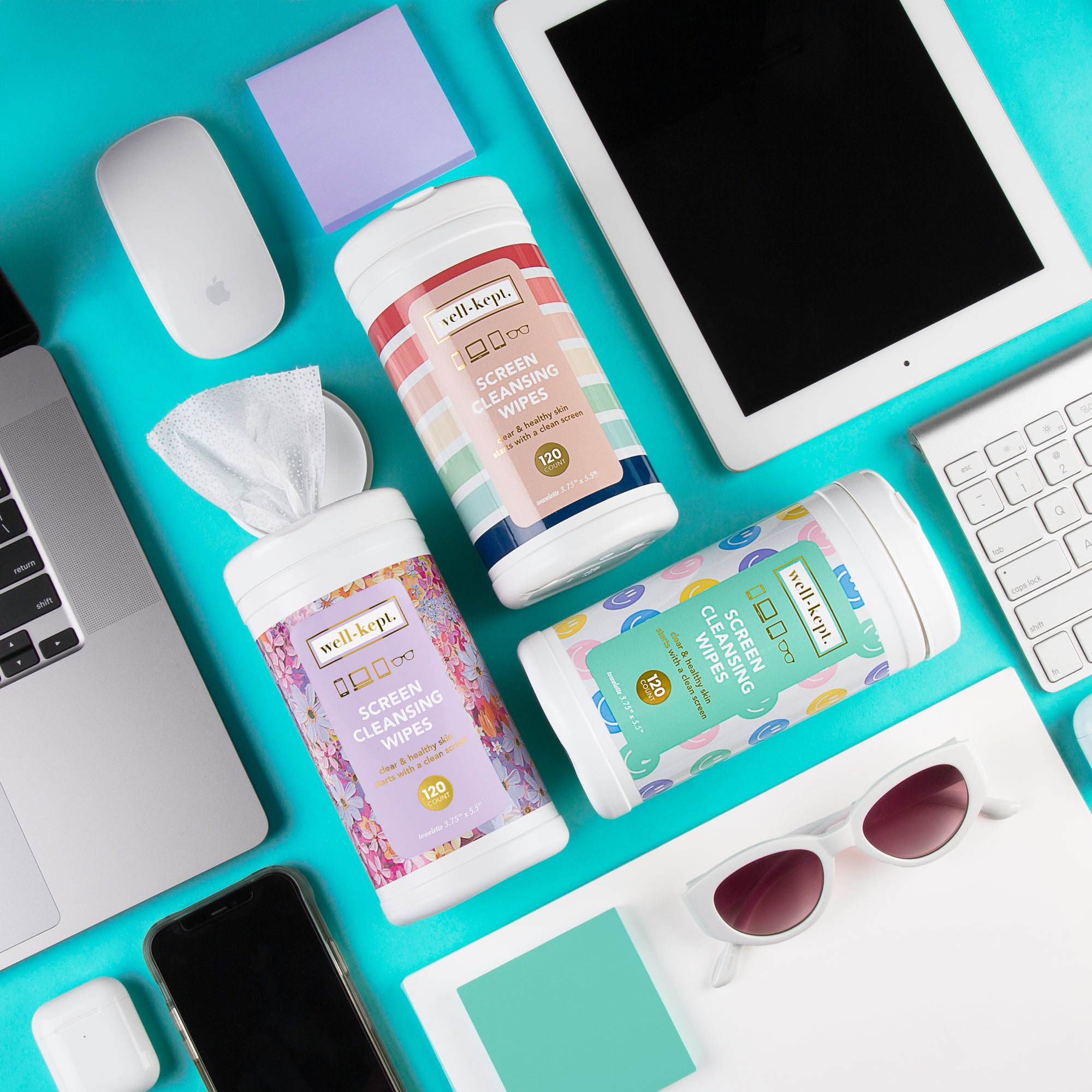 The NEW SIZE - CANISTER TRIO sits on a desk with gadgets, keyboard, mouse, phone, and sunglasses—perfect for keeping all your devices spotless.