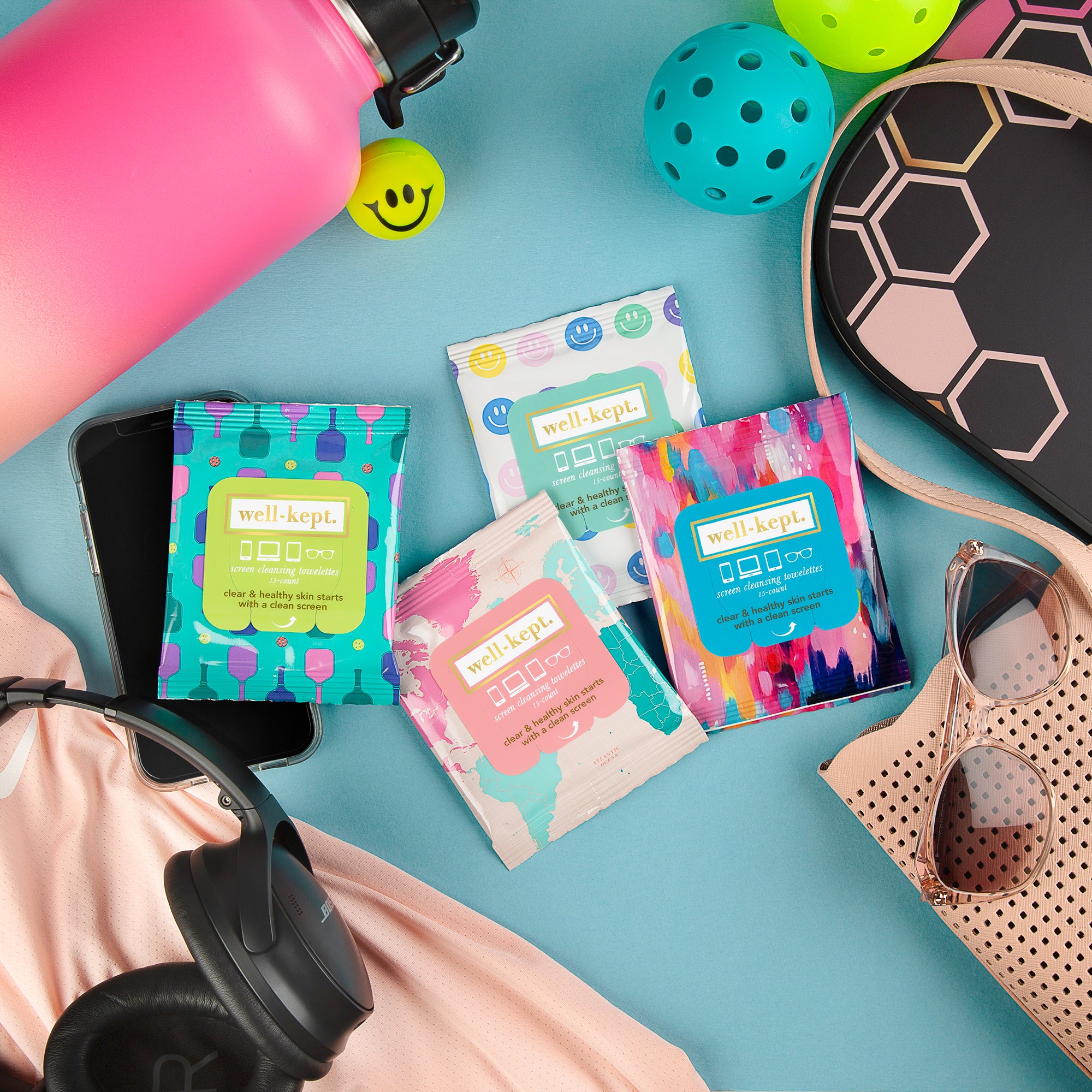 ALL SMILES screen cleaning towelettes, gym gear, sunglasses, and sports accessories arranged on a blue surface for convenient germ removal and refreshed electronics.