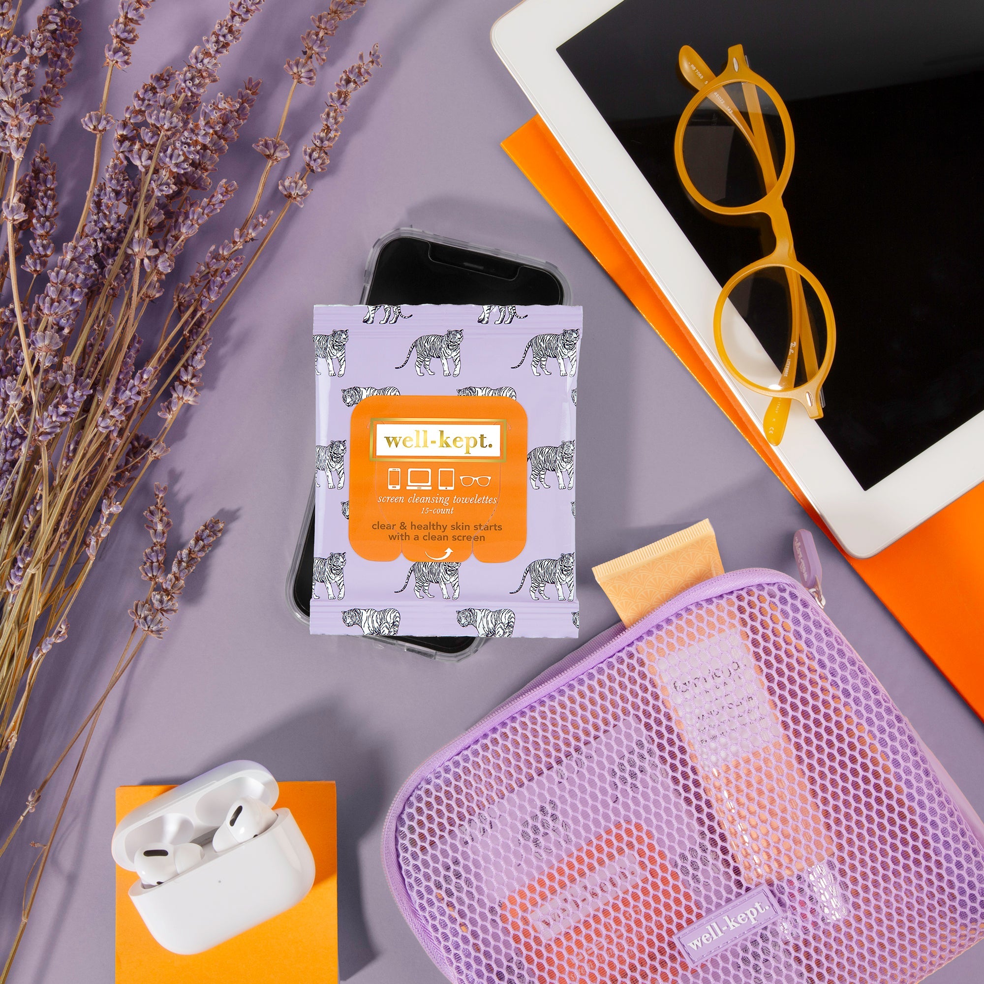 TIGER POSE - (24) Twenty Four Pack screen cleansing towelettes, iPad, yellow glasses, AirPods, and a mesh pouch rest on a lavender background with dried flowers—ideal for electronics cleaning.