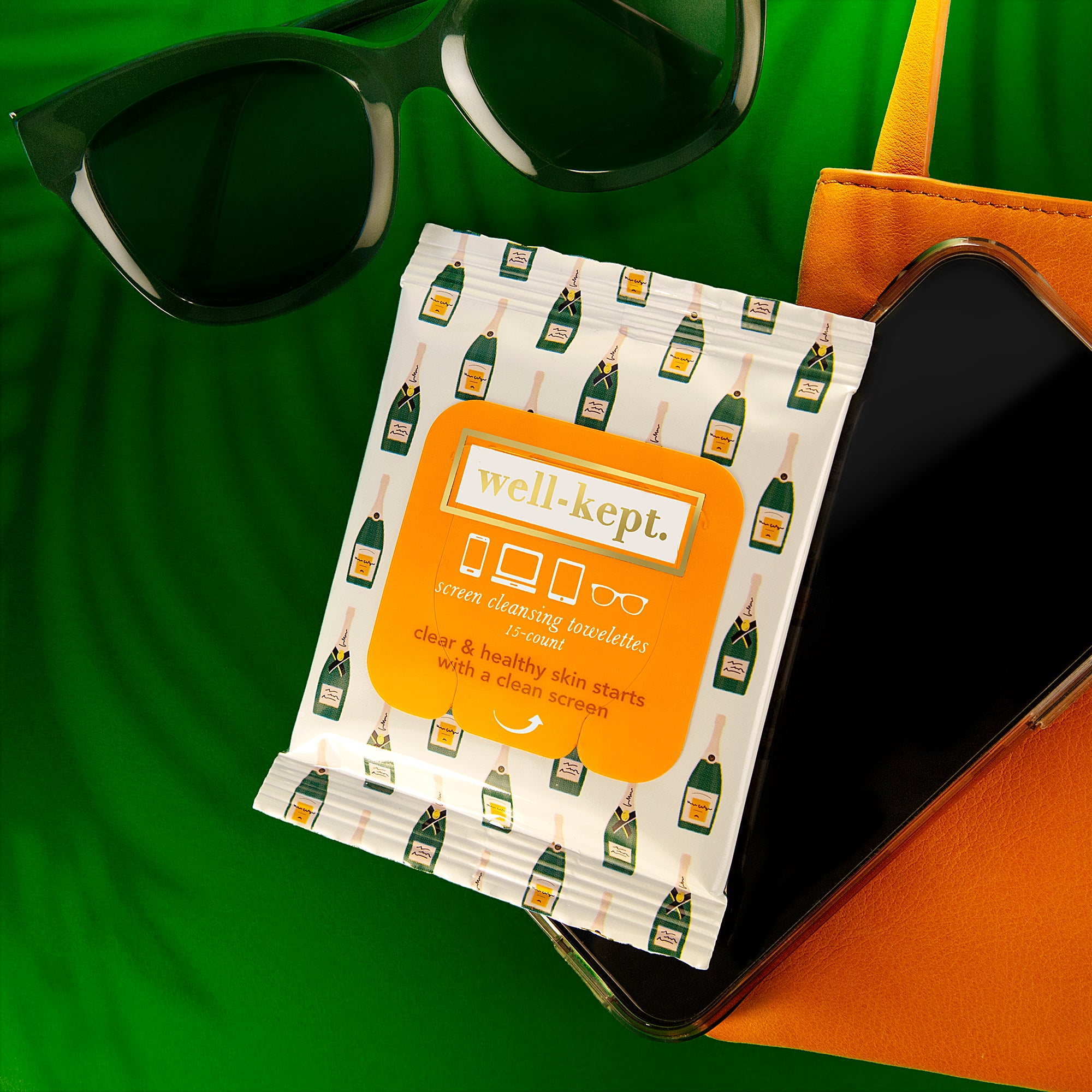 A pack of BUBBLY screen cleansing towelettes sits on a green surface, ready to remove germs from your sunglasses and phone.