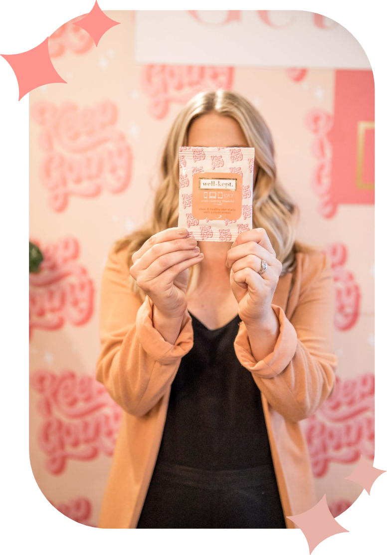 Woman in a peach blazer holds a patterned packet in front of her face against a pink-themed background.