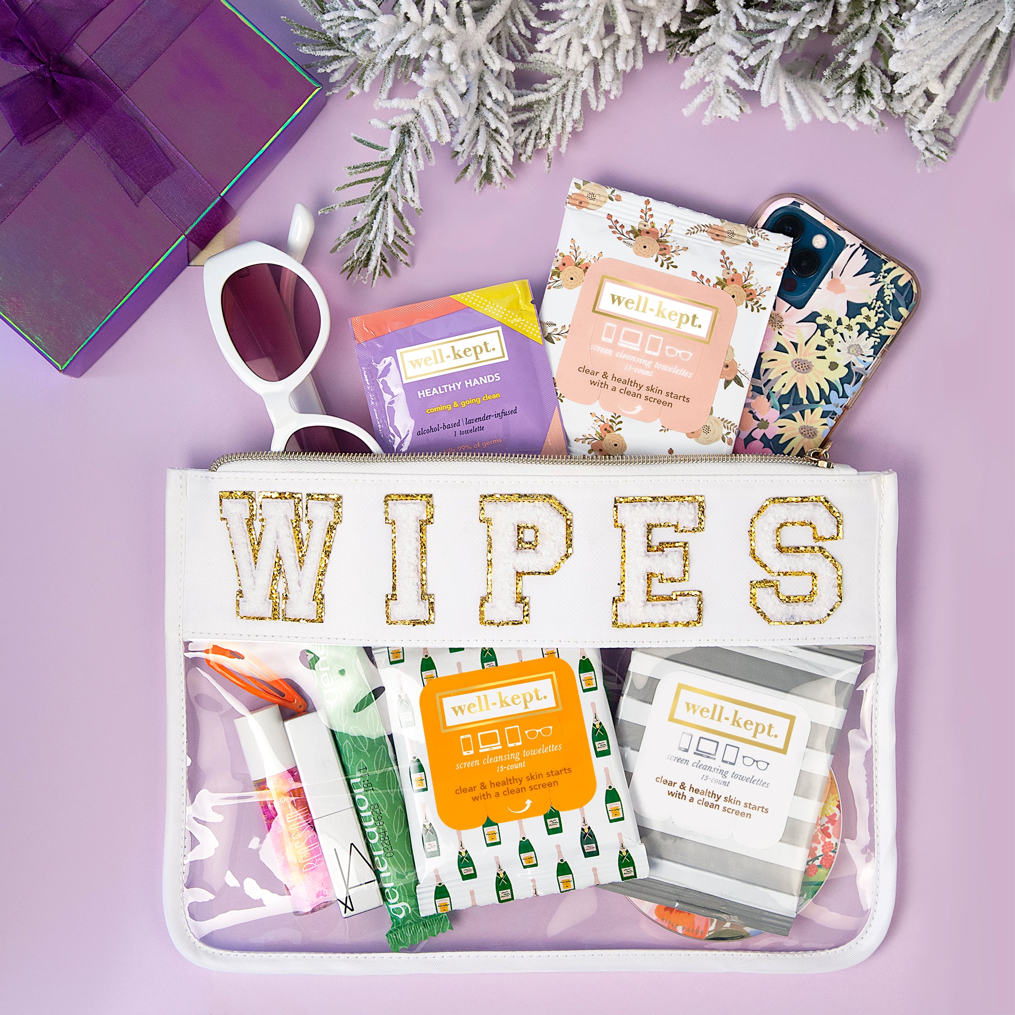 THE CLEAR WIPES POUCH is a clear PVC pouch with chenille "WIPES" letters, perfect for carrying wipes, sanitizer, sunglasses, and your smartphone. Shown on a purple background.
