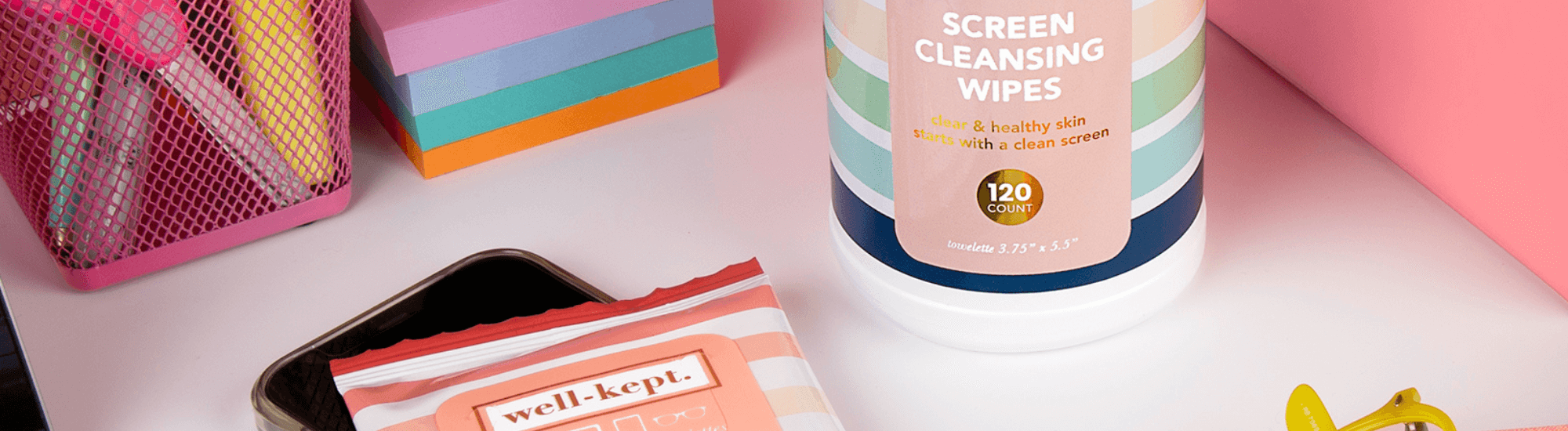 A desk with screen cleansing wipes, a pack of well-kept wipes, and office supplies on a white surface.