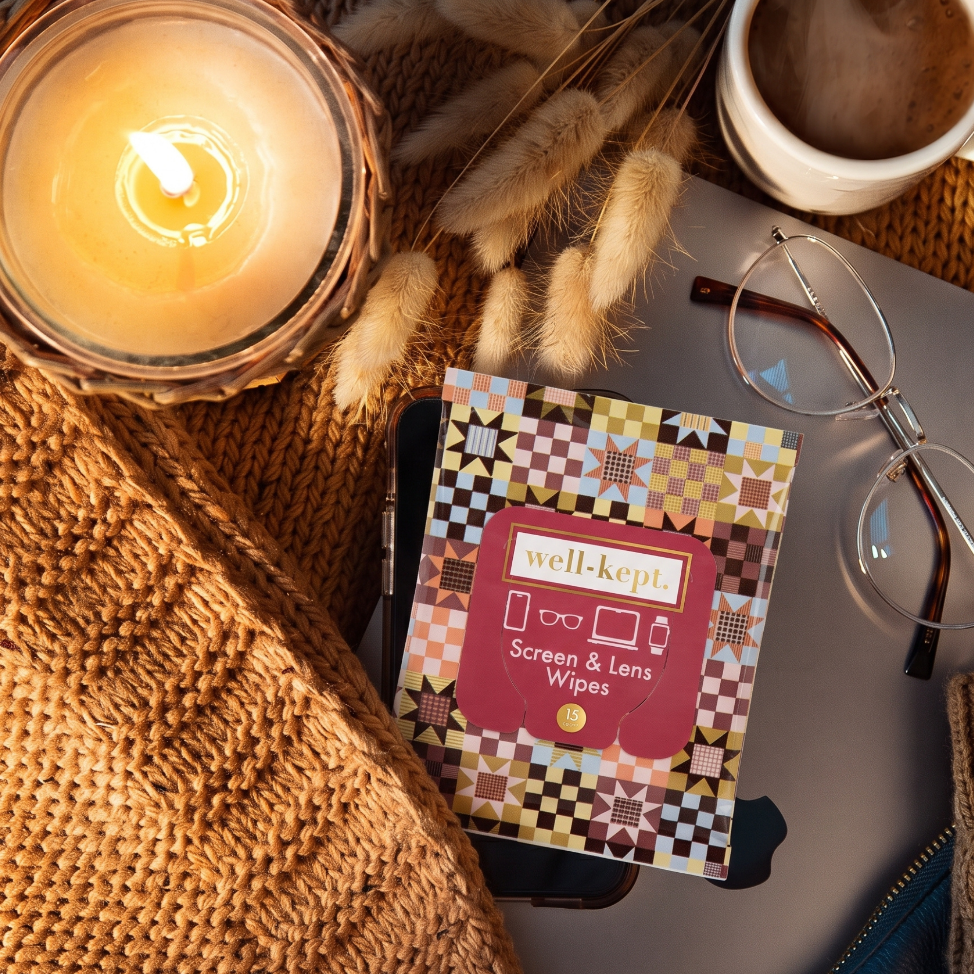 Storyteller Well-Kept screen and lens wipes pack styled with a candle, wheat sprigs, glasses, and a mug on a knit blanket
