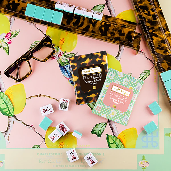 Tortoiseshell print Well-Kept screen and lens wipes pack styled in a mahjong-themed flat lay with tiles, glasses, and lemons