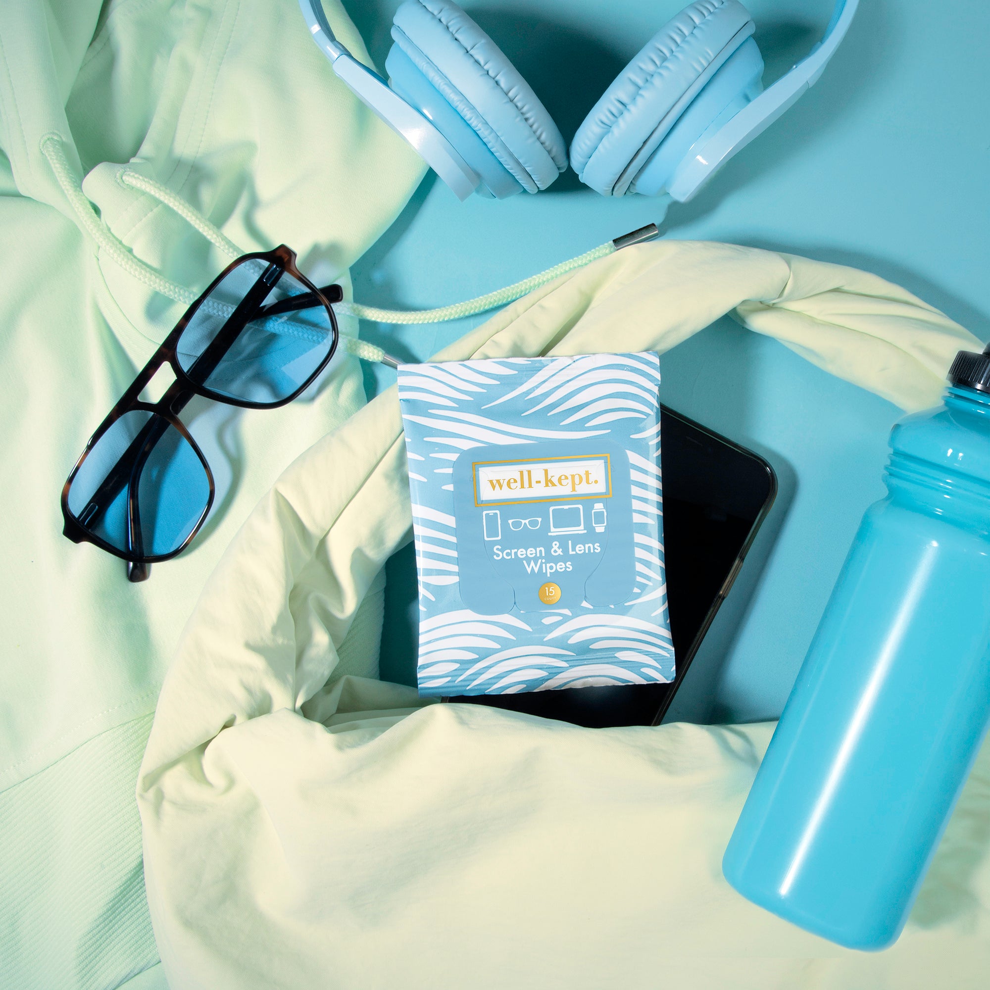 Cocoa Beach blue wave print Well-Kept screen and lens wipes pack styled with headphones, sunglasses, a phone, and a water bottle