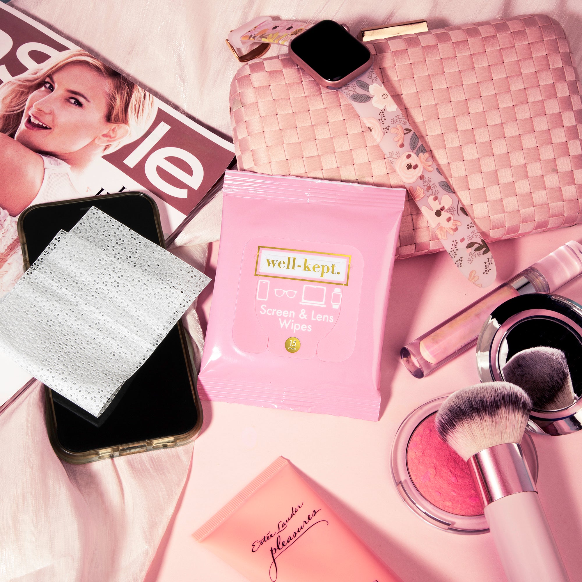 Pink Well-Kept screen and lens wipes pack styled with a phone, wipe, makeup brush, blush compact, quilted pink pouch, and a magazine